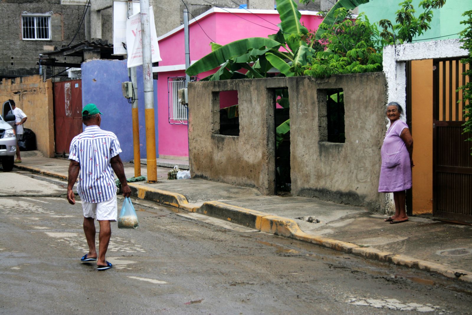 Straßenszene: Mann trägt Plastiktüte, Frau steht an Hauseingang